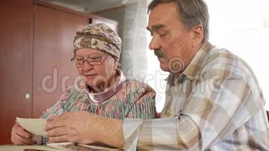 一对老年夫妇正在家里看着他们的旧照片，聊天。 有胡子的男人，有老婆的